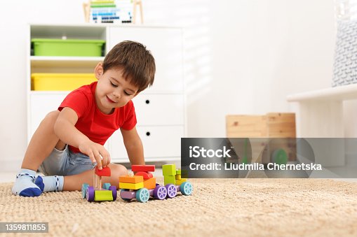 istock Cute little boy playing with colorful toys on floor at home, space for text 1359811855