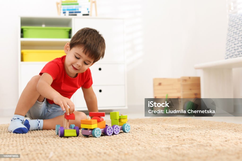 Cute little boy playing with colorful toys on floor at home, space for text Child Stock Photo