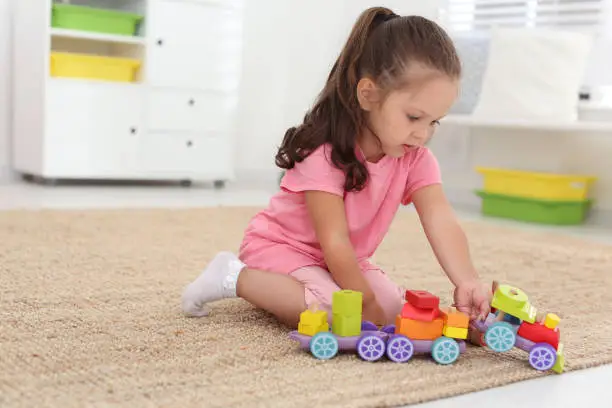 Photo of Cute little girl playing with toys on floor at home, space for text