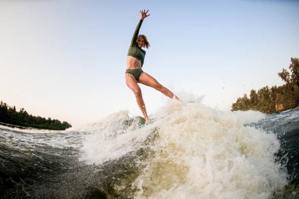 istock Smiling athletic woman balancing on wakesurf board on the river wave 1359814682