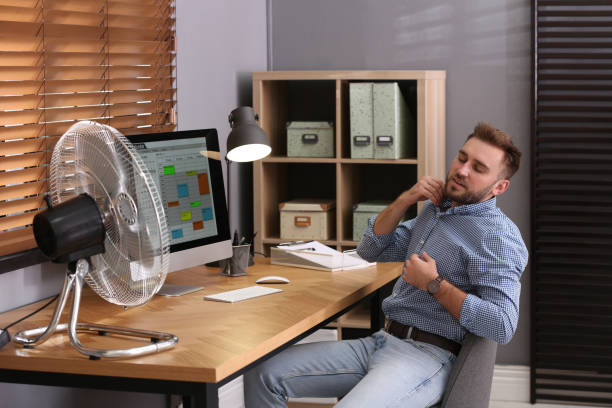 istock Man suffering from heat in front of fan at workplace 1359815077