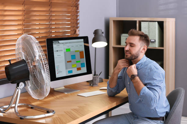 istock Man enjoying air flow from fan at workplace 1359815116