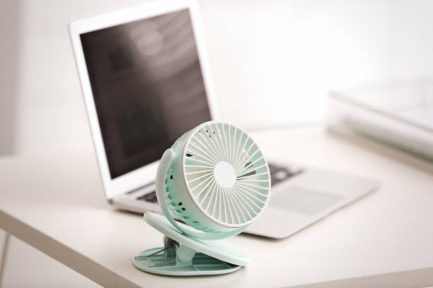istock Modern electric fan and laptop on table in office 1359815685