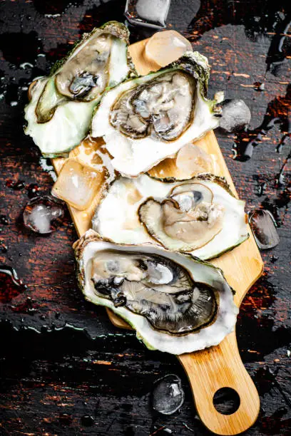 Oysters on a wooden cutting board. On a rustic dark damp background. High quality photo