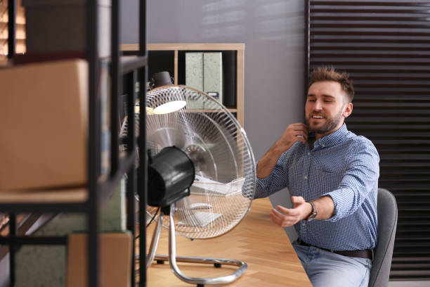 istock Man enjoying air flow from fan at workplace 1359816991