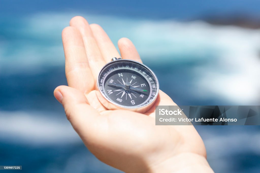 Hand holding a compass in front of the ocean Close up, Hand holding a compass in front of the ocean. Travel, concepts Human Hand Stock Photo