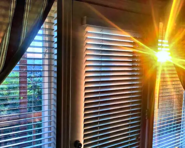 Perfect bright golden sunbeams from setting sun streaming through window blinds in home interior.