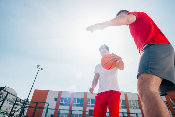 deux basketteurs caucasiens se battant pour la possession de balle sur le terrain de basket-ball par une journée ensoleillée. - building block photos et images de collection