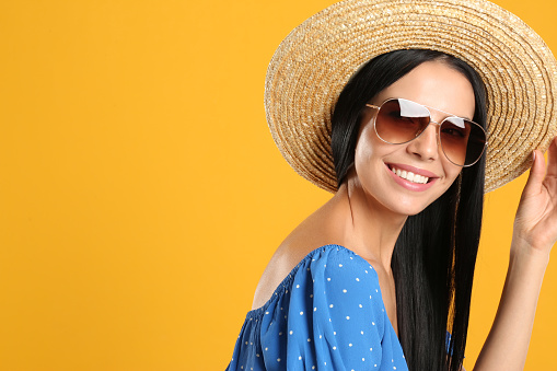 Beautiful woman wearing sunglasses on yellow background. Space for text