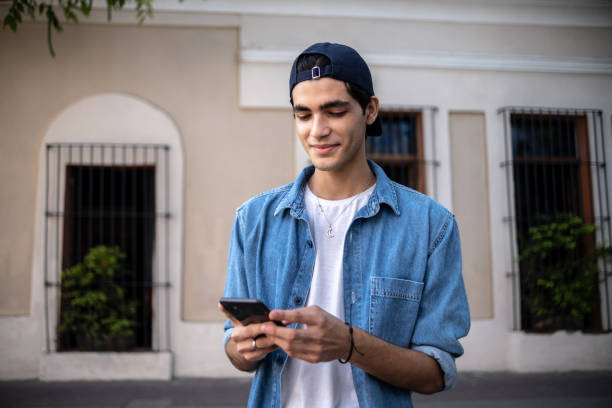мальчик-подросток пользуется мобильным телефоном на открытом воздухе - молодые мужчины стоковые фото и изображения