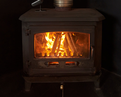 A newly lit, large Wood Burning Stove in a dark fireplace in a Devon Farmhouse