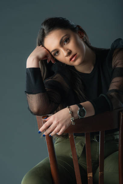 istock Attractive brunette model sitting on a old chair posing and looking at camera on grey background 1359821761
