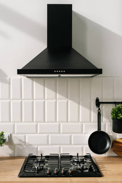 Cozy kitchen interior design with stove, pan and extractor Closeup of modern kitchen interior in white and black tones with frying pan, stove and extractor closeup. Cozy place for cooking concept. Modern household appliances kitchen hood stock pictures, royalty-free photos & images