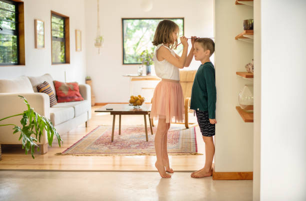 Girl measuring her younger brother's height against a wall at home stock photo