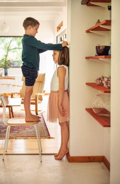 istock Boy measuring his older sister's height against a wall at home 1359825052