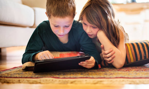 Little brother and sister using a tablet on their living room floor stock photo