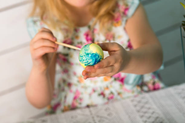 Cute little girl blonde paints colored Easter eggs with a tassel. Easter theme.