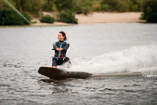 healthy sportive woman in wetsuit and vest wakeboarding on board on the river water on summer day