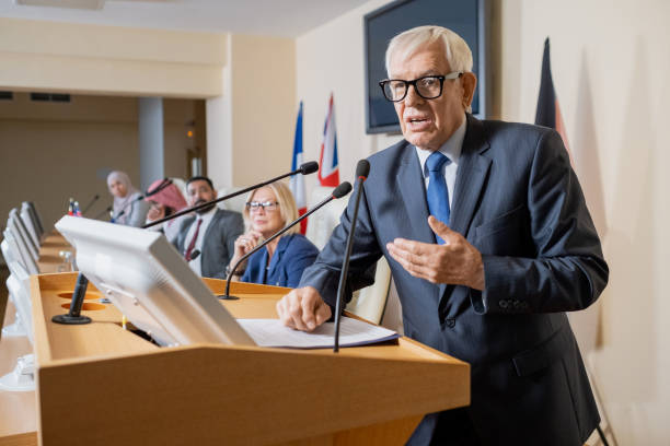 istock Confident mature delegate speaking by tribune while standing in front of audience 1359833747