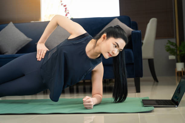 A young beautiful Asian woman learning physical exercise and workout online training program on a computer laptop at home stock photo