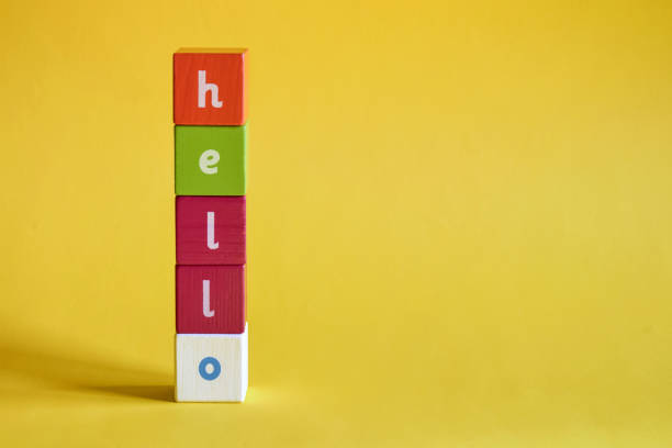 istock Word Hello made from colored wooden blocks. Painted cubes with letters are arranged vertically on yellow background. Top view. Selective focus. Copy space. 1359834726