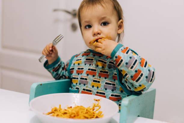 istock Cute baby eating spaghetti for dinner and making a mess. 1359835151