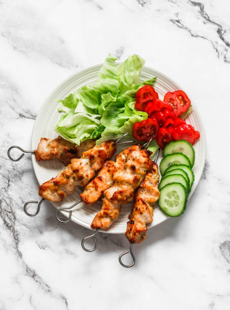 Peanut butter, yogurt and soy sauce chicken satay skewers with fresh vegetables salad on a light background, top view. Delicious tapas