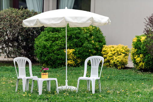 White sun umbrella, plastic two chairs and coffee table on grass in garden.