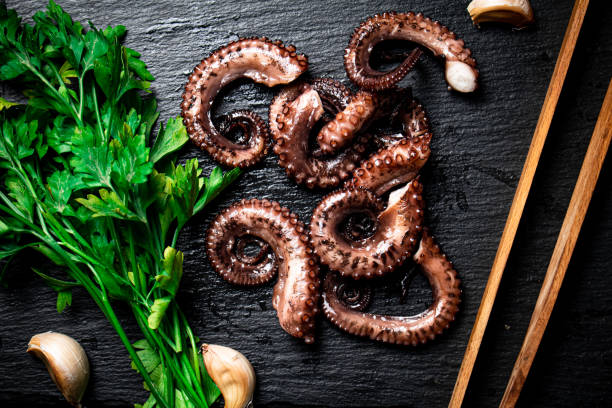 istock Pieces of fresh octopus on a stone board with greenery. 1359843794