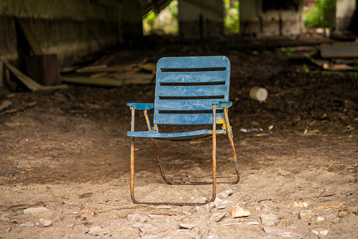 An old plastic folding chair in front of a derelict storehouse
