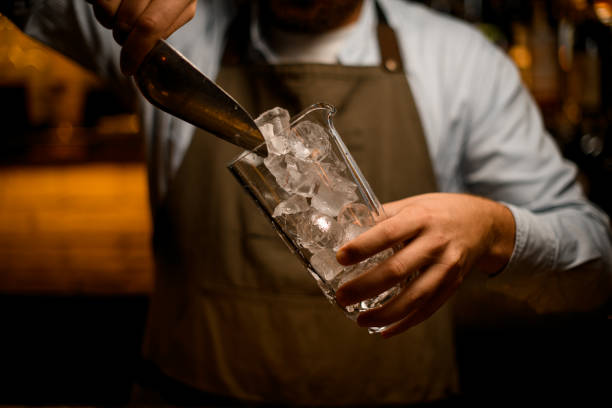 vidrio transparente en la mano del camarero y verter trozos de hielo en él con una cuchara de acero - handful fotografías e imágenes de stock