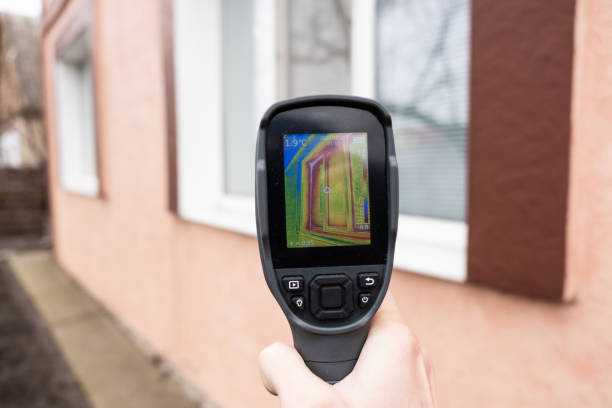 una mano masculina sostiene una cámara termográfica en la ventana de una casa. búsqueda de pérdida de calor en casas particulares - heat leak fotografías e imágenes de stock