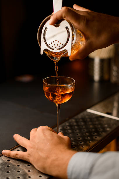 hand of bartender carefully holds strainer on mixing cup and pours liquid into wine glass stock photo