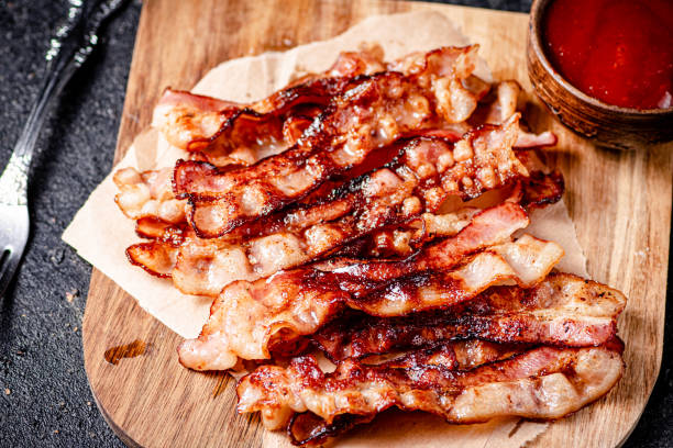 istock Pieces of fried bacon on a wooden cutting board. 1359848427