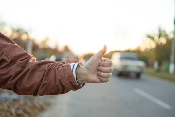 Female hand and hitchhiking sign on road, traveling by autostop in the city. Woman try stop car thumb up. Adventure and tourism concept Female hand and hitchhiking sign on road, traveling by autostop in the city. Woman try stop car thumb up. Adventure and tourism. hitchhiking stock pictures, royalty-free photos & images