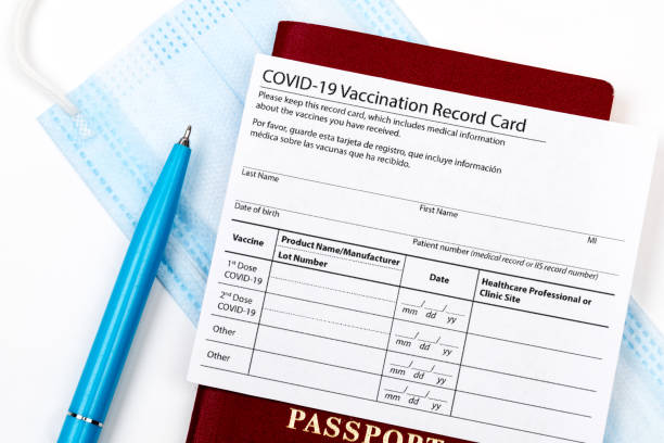 istock Coronavirus vaccination record card, biometric passport and blue medical mask on light gray desk. Concept of defeating Covid-19. Vaccination as prerequisite for travel 1359856415