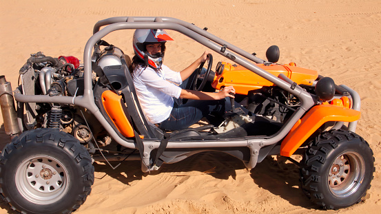 Young woman riding a buggy race car on desert