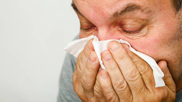 un hombre tiene un resfriado y se sopla la nariz en un pañuelo - mucosidad fotografías e imágenes de stock