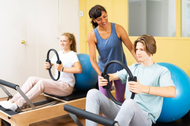 les adolescents effectuent des exercices avec un anneau de gymnastique sous la direction de l’entraîneur - pilates machine photos et images de collection