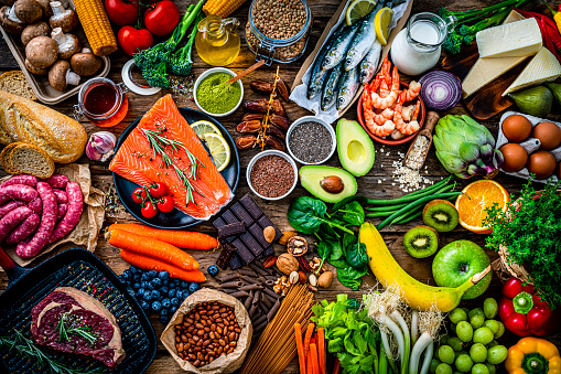 Food and drink backgrounds: large group of raw food that includes fruits, vegetables, raw salmon, sardines, beef meat, sausages among others shot from above on dark rustic table. High resolution 42Mp studio digital capture taken with SONY A7rII and Zeiss Batis 40mm F2.0 CF lens