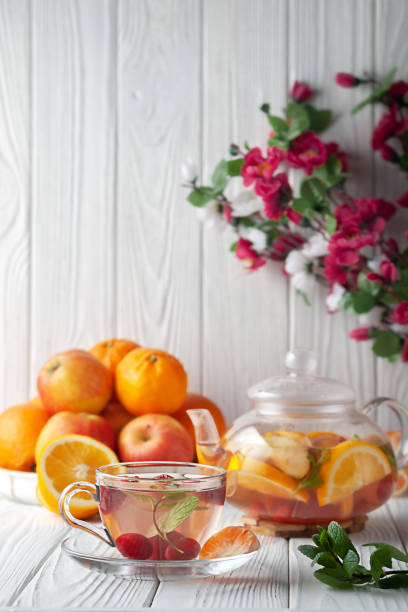 istock Fruit tea with berries, oranges and mint in a glass teapot on a white background 1359862948