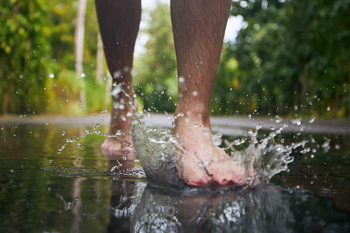 Barefoot leg of young man stepping to puddle and splashing water during rainy day.\