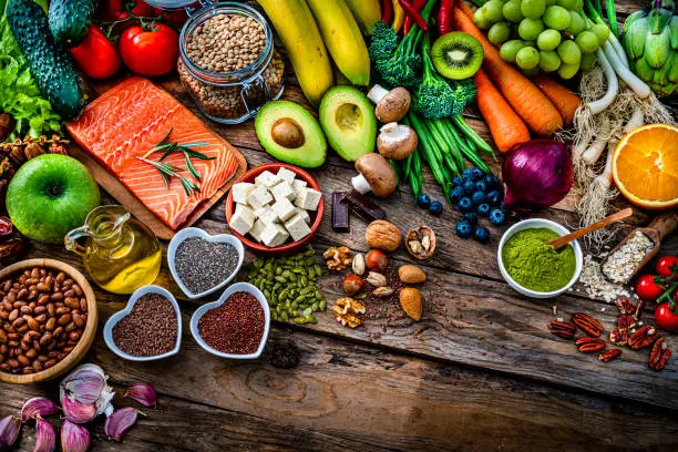 Food backgrounds: high angle view of a large group of raw healthy food for heart care that includes fruits, vegetables, raw salmon, beans, legumes, tofu, flax seed, chia seed, berries, oat, nuts, moringa powder shot on rustic wooden table. High resolution 42Mp studio digital capture taken with SONY A7rII and Zeiss Batis 40mm F2.0 CF lens