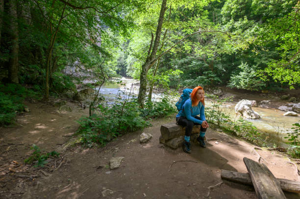 istock Woman relaxing alongside river while sitting on a tree stump 1359867476