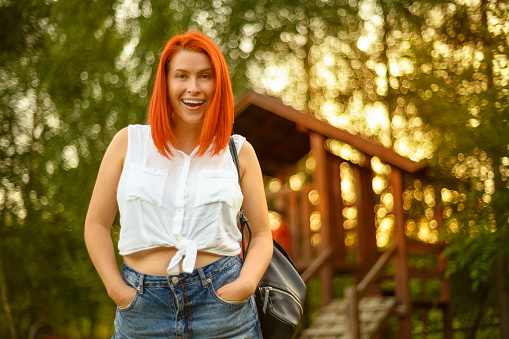 front view close up caption with red hair, tooth smiling woman in light outfit in park on a summer day