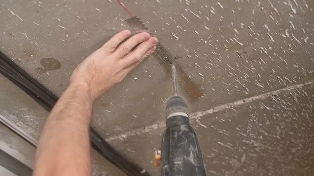 Worker drills a hole in the ceiling with a hammer drill to install the ceiling profile fixing. Installation of plasterboard ceiling. Renovation or reconstruction of the building. Close-up, live video