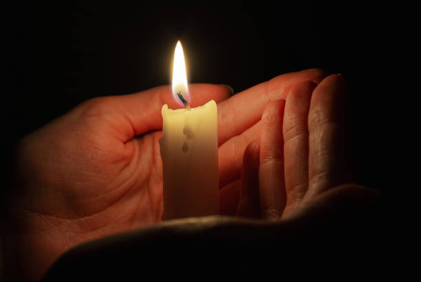 istock Burning candle in woman's hands in dark 1359873315