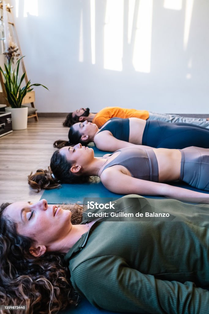 Group meditating in Corpse pose Women and men with closed eyes lying on floor in Shavasana pose and meditating during group yoga session in studio Lying Down Stock Photo