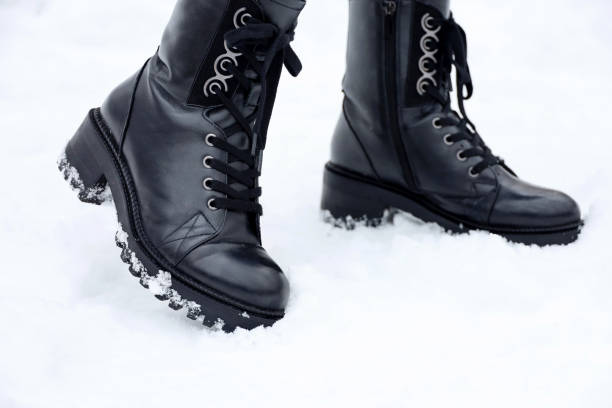 istock Female legs in black leather lace-up boots on a snow 1359873534