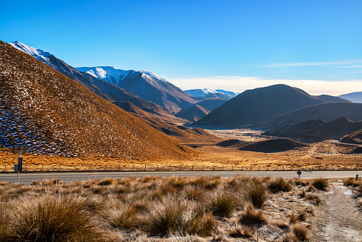 Driving through the golden tussock terrain of the Alpine Pass with a dusting of snow on the hills